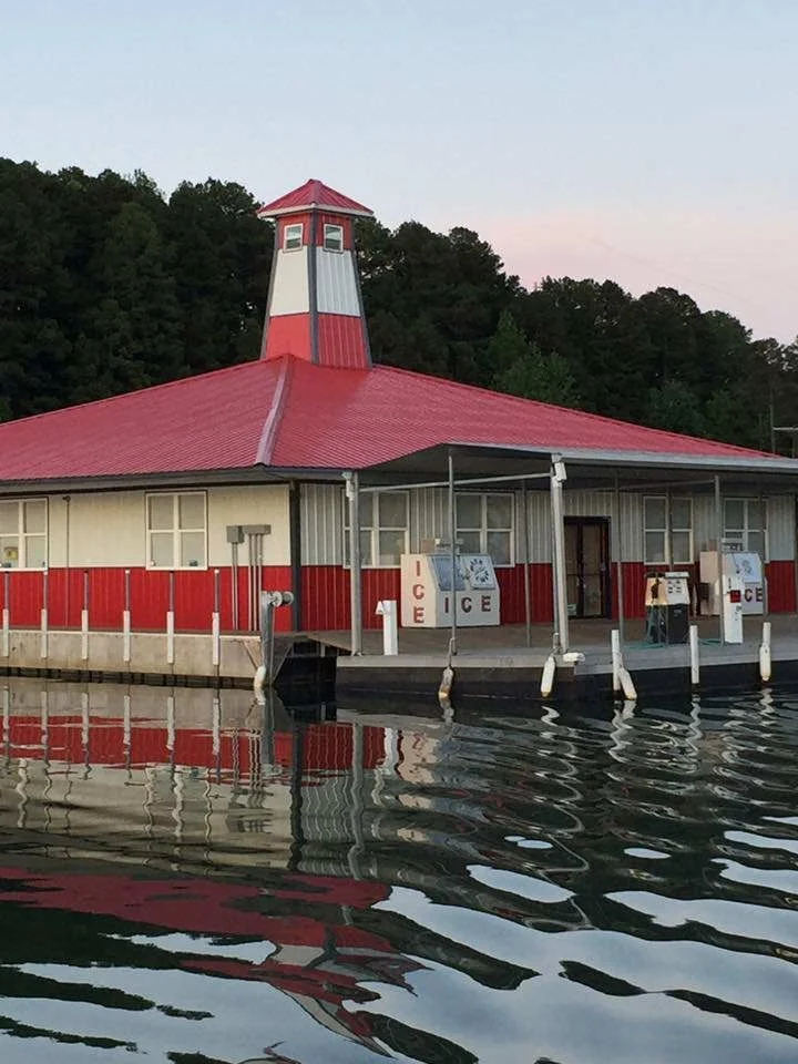 Red-roofed marina building with a lighthouse-style tower, with ice machines and fuel pumps on the dock